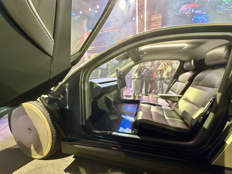 Interior of a Tesla Cybercab seen through its open butterfly door: two seats, a center touchscreen and no steering wheel or pedals